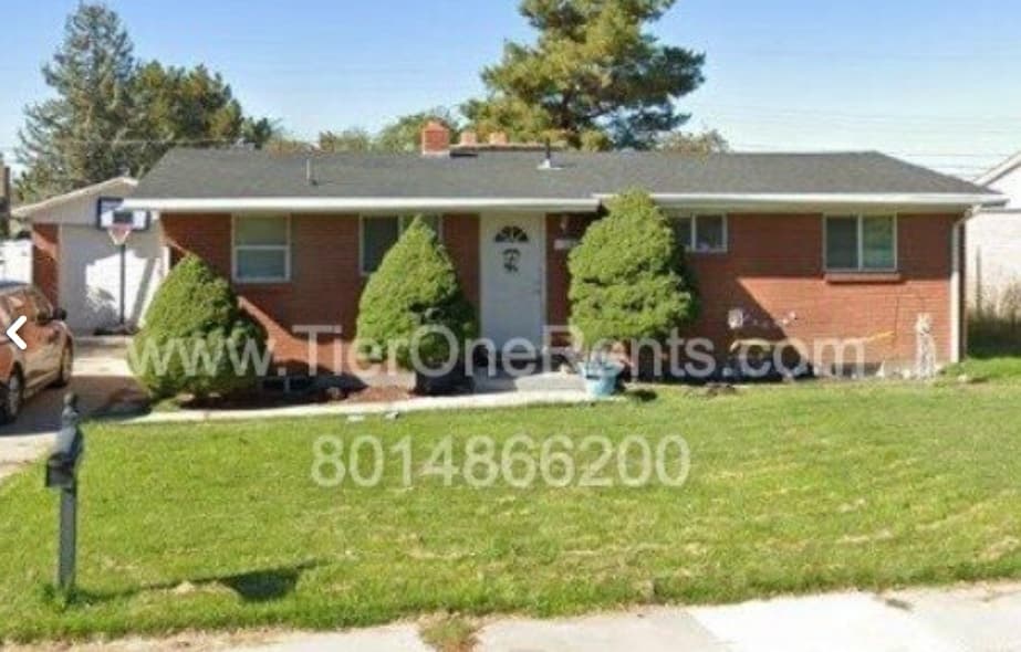 A one-story red brick house with a dark roof, trimmed bushes in front, a white front door, and a grass lawn. Cherry Hill Apartments Orem and TierOneRents.com with a phone number are displayed across the center of the image.