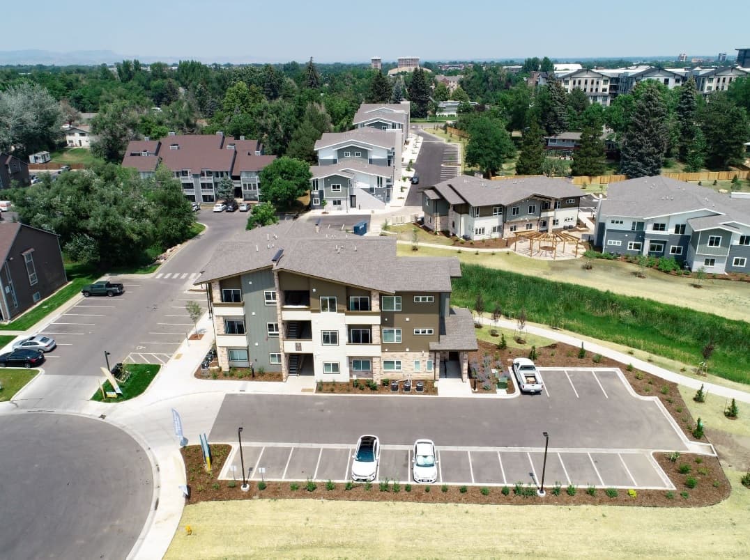 Aerial view of Bighorn Landing Fort Collins, a residential apartment complex with multiple buildings, parking lots, green lawns, trees, and nearby roads on a clear day.