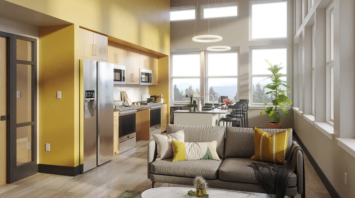 Modern kitchen and living room at Ferry Street Flats Eugene with tall windows, yellow accent wall, gray sofa with colorful pillows, stainless steel appliances, indoor plants, and a dining area bathed in natural light.