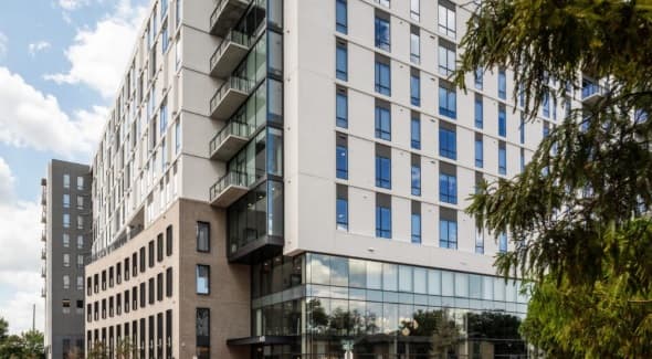 Otto Northgate is a modern multi-story apartment building with large glass windows, balconies, and a mix of brick and white exterior. A tree stands in the foreground beneath the partly cloudy sky.