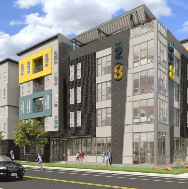 Modern four-story apartment building with large windows, colorful yellow and teal accent panels, and the word “COLAB” on the exterior. Live at CoLab Denver—people stroll by on the sidewalk as a car is parked on the street in front.